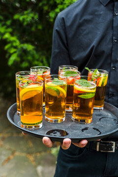 Server holding Pimm's cocktails at an outdoor event.