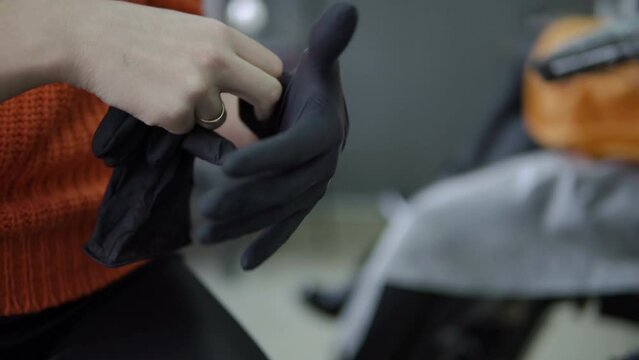 The girl is wearing black rubber gloves. The tattoo master prepares to apply the drawing. the cook in the kitchen uses black gloves. The cosmetologist pulls on the gloves. Illegal transplantology.