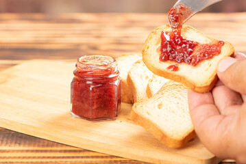 Jam and toast, hand spreading jam on toast with knife on rustic wood. Selective focus.
