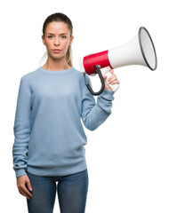 Beautiful young woman holding megaphone with a confident expression on smart face thinking serious