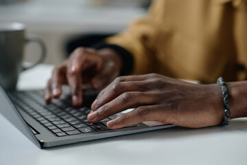 Closeup of hands of african american man typing on laptop keyboard while sitting at desk