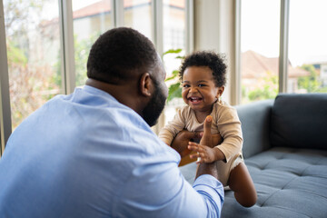 Portrait Of Happy African American Dad With Cute Little Baby Girl on couch at home in the living...