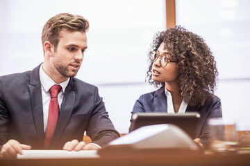 Woman of African descent in business attire and her colleagues sitting at desk having a meeting an a large office. Cape Town, South Africa