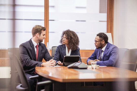 Woman of African descent in business attire and her colleagues sitting at desk having a meeting an a large office. Cape Town, South Africa