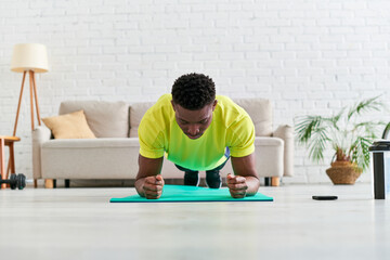 african american man in sportswear training in plank pose on fitness mat in modern living room