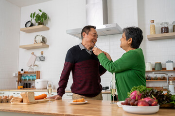 Mature couple have spending time with tasting sausage together in kitchen