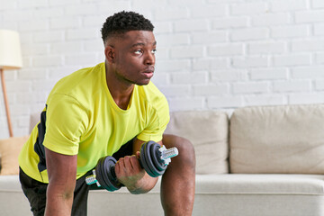confident african american man in sportswear working out with dumbbell on fitness mat at home
