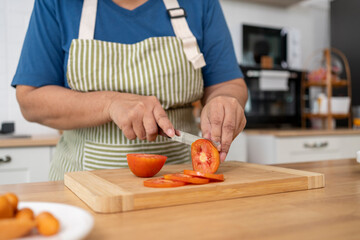 Hands of Senior woman cutting tomato for preparing cooking in kitchen