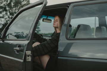 A redheaded girl in a green sweater sits in a retro car. The concept of free and cyclical fashion.
