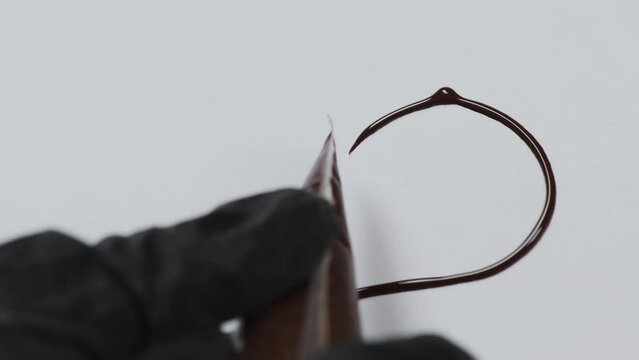 Chef artfully uses piping bag filled with chocolate to paint heart-shaped pattern. Confectioner displays proficiency in drawing on paper during culinary class