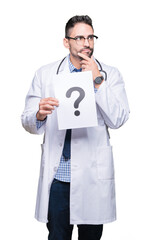 Handsome young doctor man holding paper with question mark over isolated background serious face...