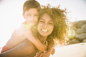 Mixed race mother carrying her son on her back at the beach while playing.