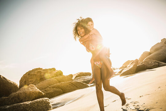 Mixed race mother carrying her son on her back at the beach while playing.