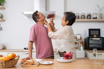 Mature asian Couples playfully tease each other with grapes in kitchen.