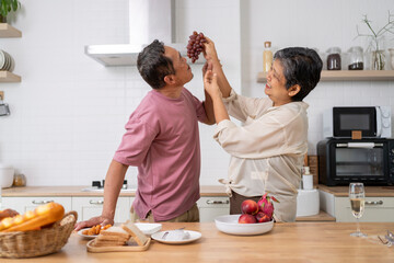 Mature asian Couples playfully tease each other with grapes in kitchen.
