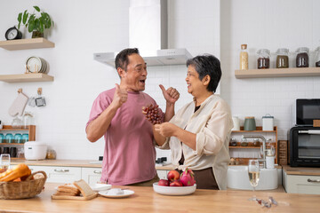 Mature asian Couples playfully tease each other with grapes in kitchen.