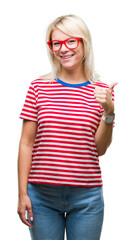 Young beautiful blonde woman wearing glasses over isolated background doing happy thumbs up gesture with hand. Approving expression looking at the camera with showing success.