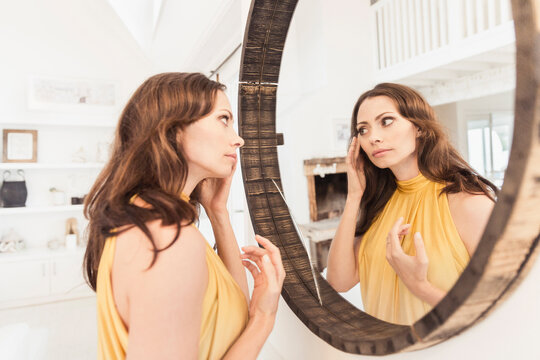 Beautiful woman putting on ear rings while looking at a mirror