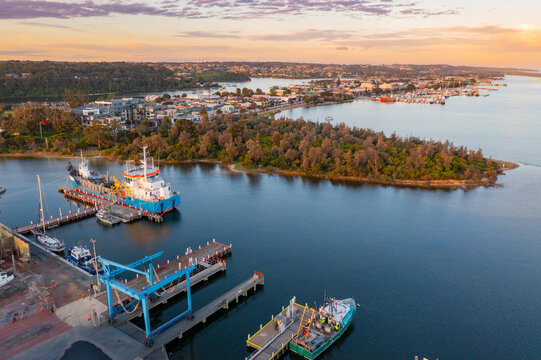 Aerial view of a ship at a wharf alongside a ship repair dock and waterfront area at sunset