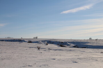 A flat landscape with a snowy field and trees in the background