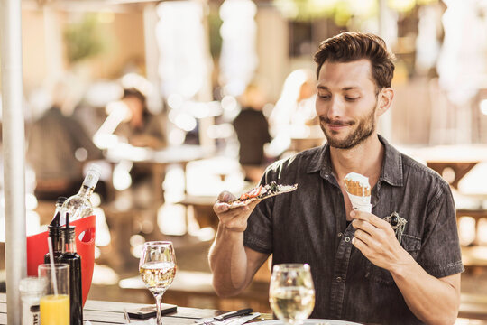 Man in an outdoor restaurant trying to decide between pizza or ice cream.