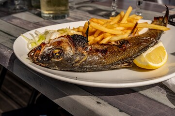 Cooked fish on table. Grilled sea bream with fries and lemon.