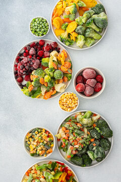 Preparing fresh vegetables in summer for winter, various frozen vegetables and berries in plates on a gray background, top view