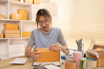 Sell products online, Woman is writing down the customer's details and addresses on box in order to prepare for shipping according to the information, Packing box, Sell online.