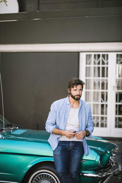 Cool looking dude sitting on his vintage convertible sports car.