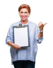 Senior caucasian business woman holding clipboard over isolated background pointing and showing with thumb up to the side with happy face smiling
