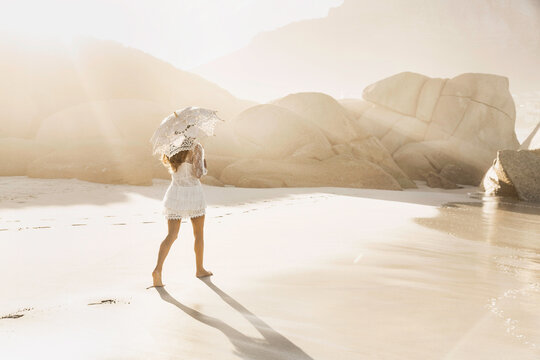 Beautiful girl in white summer dress dancing and playing on the beach