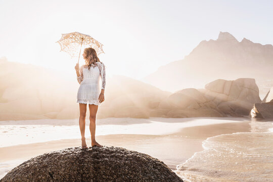 Beautiful girl in white summer dress dancing and playing on the beach