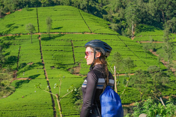 Pretty beautiful girl cyclist in a helmet and sunglasses stands against the backdrop of hills during a bike ride