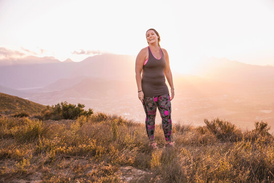 Beautiful overweight woman exercising on a mountain at sunset
