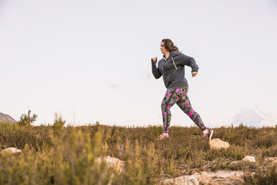 Beautiful overweight woman exercising on a mountain at sunset