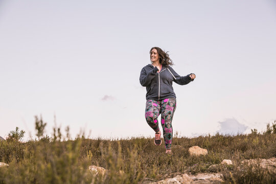 Beautiful overweight woman exercising on a mountain at sunset