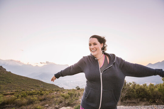 Beautiful overweight woman exercising on a mountain at sunset