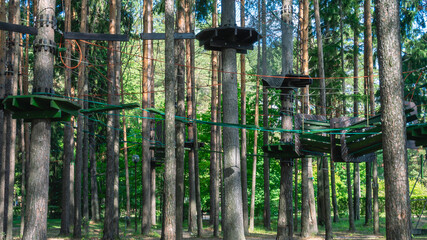 A rope park for children among the trees in summer. The entertainment complex is at a height. An attraction for outdoor activities. Entertainment for children and adults in the forest