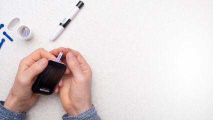 Caucasian middle aged man hands to make home testing with glucose meter over table with strips and...