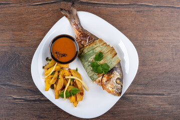 Top view of baked dorado fish and potatoes with bamboo shoots and Sichuan sauce on a white plate.