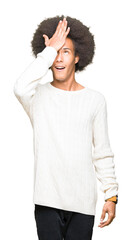 Young african american man with afro hair wearing winter sweater surprised with hand on head for mistake, remember error. Forgot, bad memory concept.