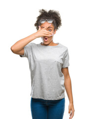 Fototapeta na wymiar Young afro american woman wearing glasses over isolated background peeking in shock covering face and eyes with hand, looking through fingers with embarrassed expression.