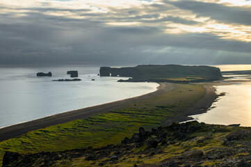 Scenic view of the black lava sand of Dyrhólaey beach with its giant cliffs at sunset with...