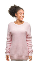 Young afro american woman wearing winter sweater over isolated background looking away to side with smile on face, natural expression. Laughing confident.