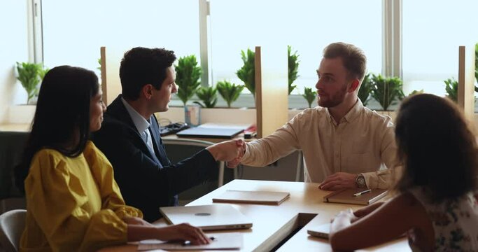 Young Caucasian and Hispanic businessmen, partners shake hands finish formal meeting in office conference room, establish partnership, make commercial deal, feel satisfied with successful cooperation
