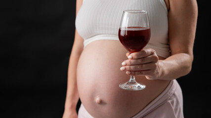 Close-up of the belly of a pregnant woman holding a glass of red wine on a black background. 