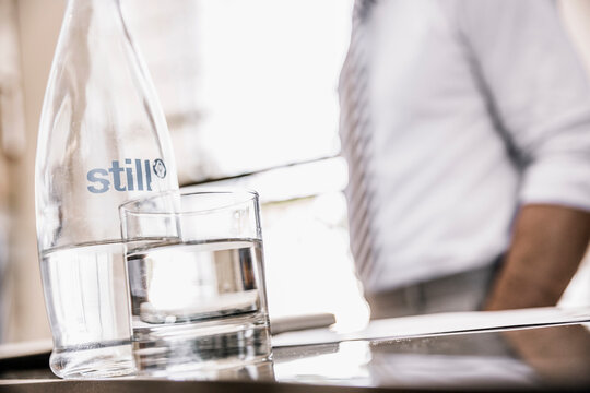 Glass of bottled water and glass on a desk with businessman in the back slightly out of focus