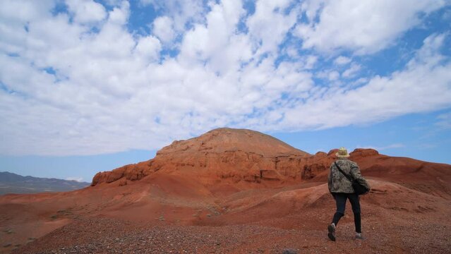A tourist guy walks in a canyon of unusual red rocks. Mountains and rocks made of red sandstone. Azhirzhar tract, Kazakhstan.