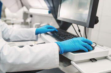Laboratory technician in rubber gloves performs series of tests in bio laboratory. Doctor takes tests on chemical analyzer, closeup without face. Working at computer in modern laboratory
