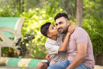 Happy indian son kissing his father while sitting at park - concept of affectionate, family...